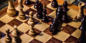 Imagem com um tabuleiro de xadrez, no qual há alguns peões e o rei está caído. Essa imagem simboliza a estratégias de gestão Qualidade.
