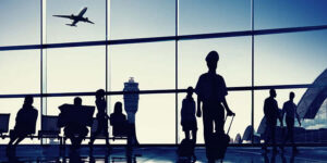 Várias pessoas em um aeroporto caminhando com um avião passando pela janela. Essa imagem simula a experiência do cliente.