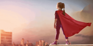 Essa imagem tem uma criança com uma capa improvisada de super herói, olhando para frente e com a mão apontando para cima. Essa imagem simboliza a importância da autonomia.