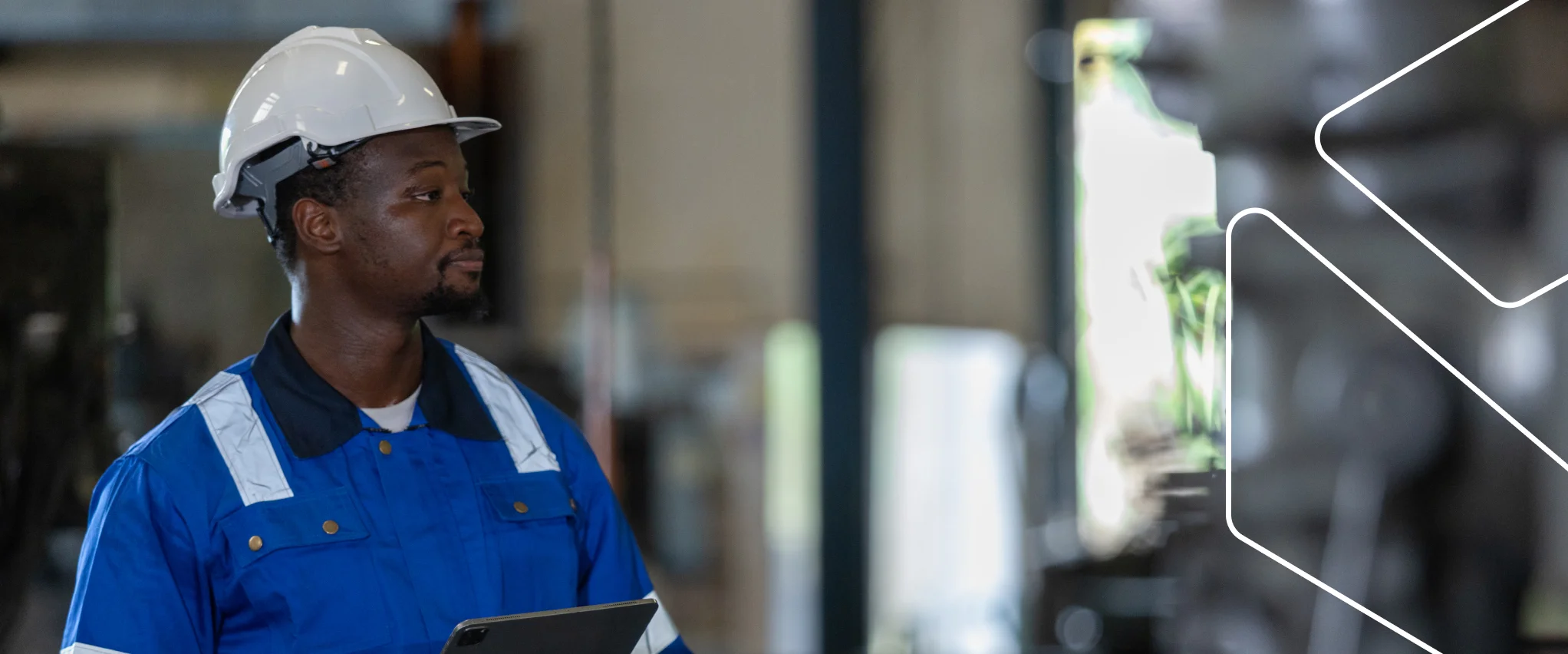 Profissional com capacete e uniforme azul usa um tablet para acompanhar o sistema de gestão da qualidade em ambiente industrial